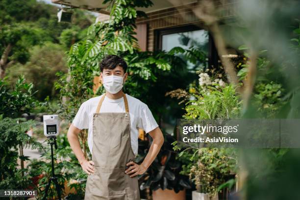 porträtt av självsäker ung asiatisk manlig florist, ägare av småföretagsblombutik som bär skyddande ansiktsmask för att förhindra spridningen av coronavirus, stående på butiksfronten. återöppning efter covid-19-koncept - butiksinvigning bildbanksfoton och bilder