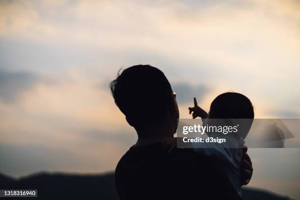 silhouette of a loving young asian father holding little daughter in arms, looking towards beautiful sunset while little daughter points off into the sky. enjoying quality family bonding time together. family love and lifestyle - innocence project stock pictures, royalty-free photos & images