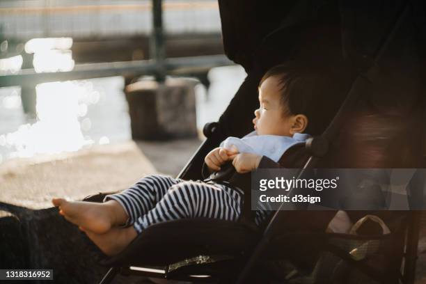 adorable little asian baby girl sitting on baby stroller against beautiful sunset by the sea. family love and lifestyle - kinderwagen stockfoto's en -beelden