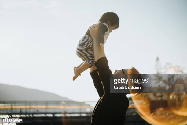 a loving young asian father lifts her little daughter up in the air. enjoying a moment and spending quality family bonding time together against beautiful sunset in park. family love and lifestyle - carefree moment stock pictures, royalty-free photos & images
