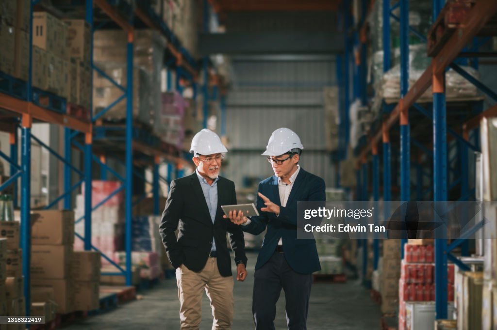 Gestión china asiática teniendo discusión en el almacén con hardhat blanco usando tableta digital