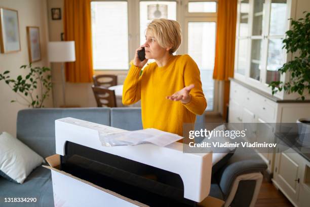 donna che usa un telefono cellulare e tiene una mano a metà strada per disimballare il suo acquisto online - complaining foto e immagini stock