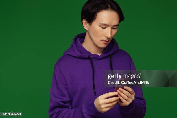 emotional asian man wearing hoodie with smart phone - man and his hoodie imagens e fotografias de stock