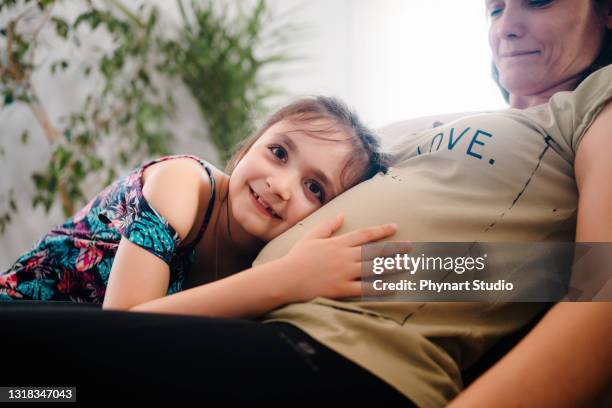 nieuwsgierig meisje dat haar zwangere moederbuik observeert - belly kissing stockfoto's en -beelden