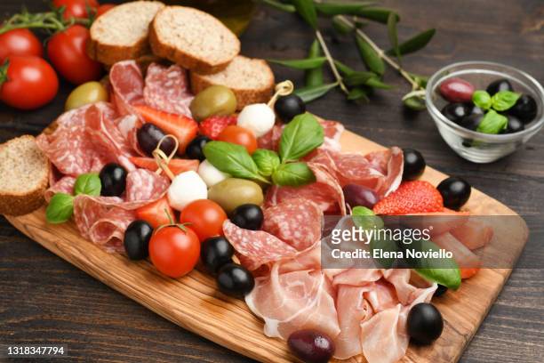 charcuterie board salami, prosciutto, with green and black olives, appetizers with mozzarella balls, cherry tomatoes and strawberries. - charcutería fotografías e imágenes de stock