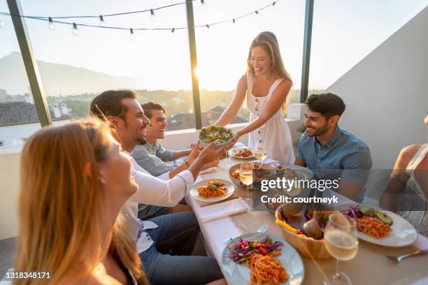 friends and family passing salad on a table at sunset. - rooftop dinner stock pictures, royalty-free photos & images
