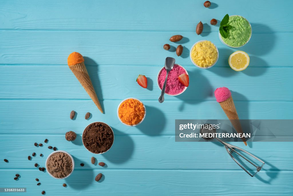 Assorted ice cream cups in a row and waffle cones colorful on blue wood background