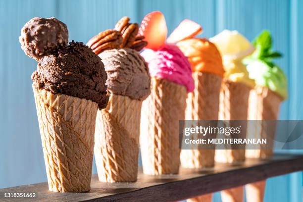 assorted ice cream waffle cones in a row colorful different flavor on pink and blue wood - mint chocolate chip ice cream scoop stock pictures, royalty-free photos & images