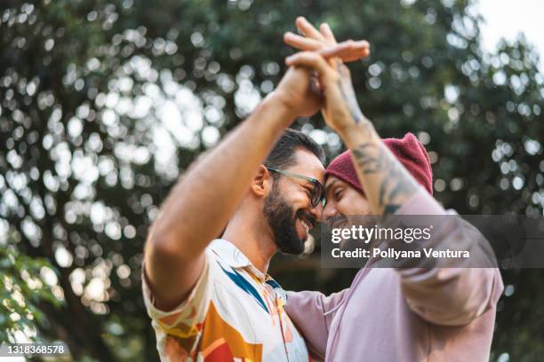 schwules paar berührt hände im öffentlichen park - couples romance stock-fotos und bilder
