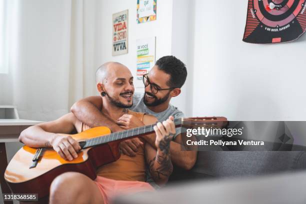 casal gay tocando guitarra e cantando no sofá - gay person - fotografias e filmes do acervo