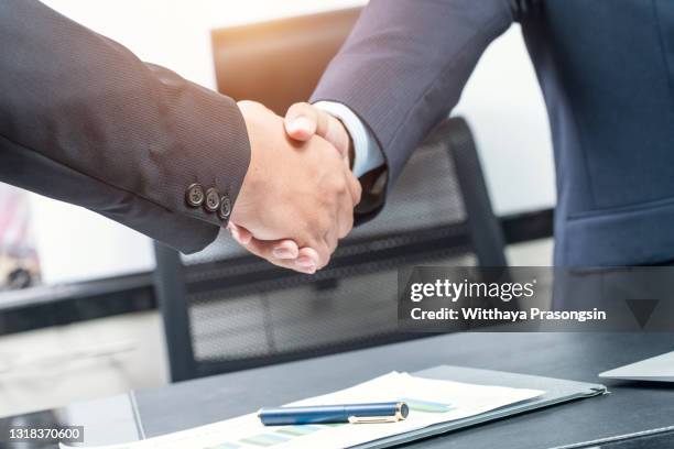 good deal. close-up of two business people shaking hands while sitting at the working place - fusions et acquisitions photos et images de collection