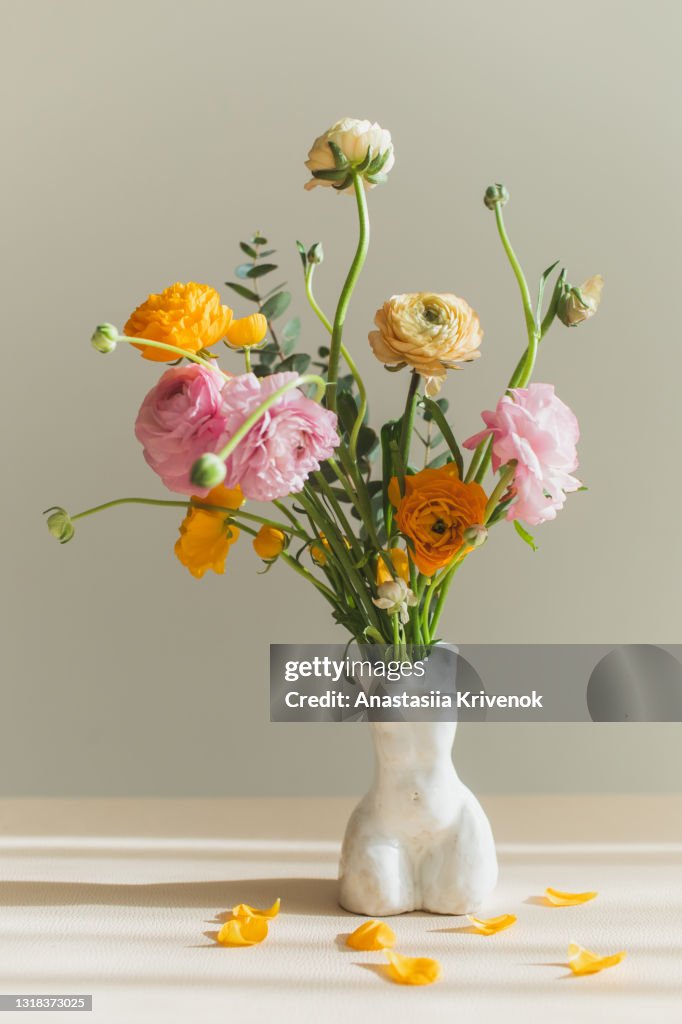 Ranunculus flower bouquet standing in woman's bodie shaped ceramic vase.