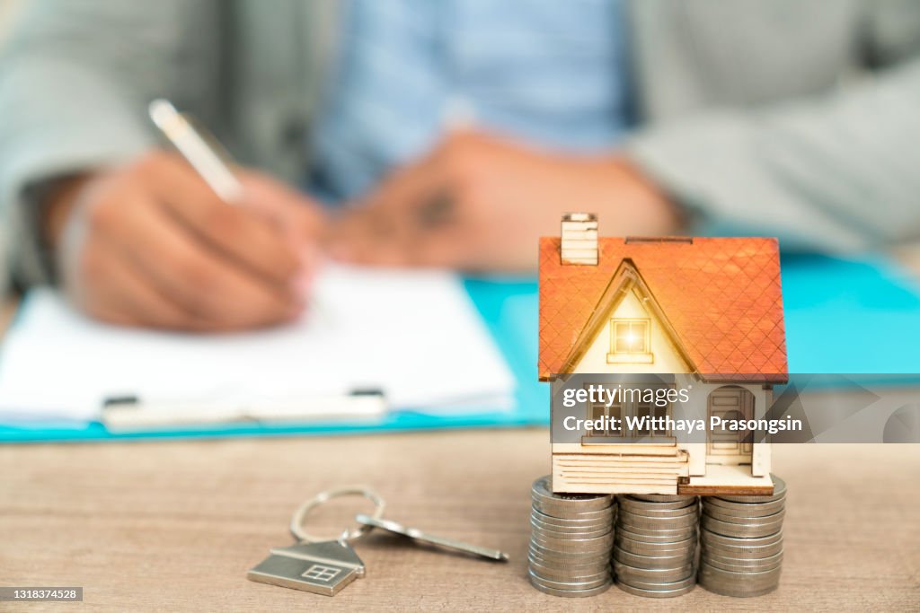 Real estate concept - businessman signs contract behind home architectural model