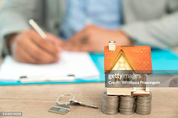 real estate concept - businessman signs contract behind home architectural model - debt photos et images de collection