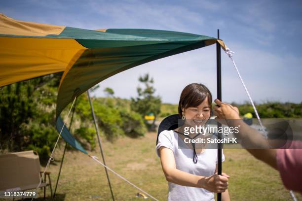 young woman holding a pole to set up tarpaulin - tarpaulin stock pictures, royalty-free photos & images