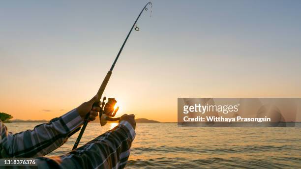 fishing rod wheel closeup, man fishing with a beautiful sunrise behind him - fishing reel foto e immagini stock