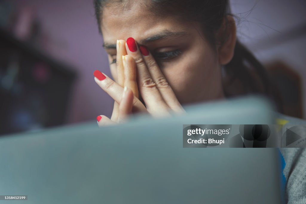 Gestresste junge Frau mit einem Laptop, um von zu Hause aus zu arbeiten.