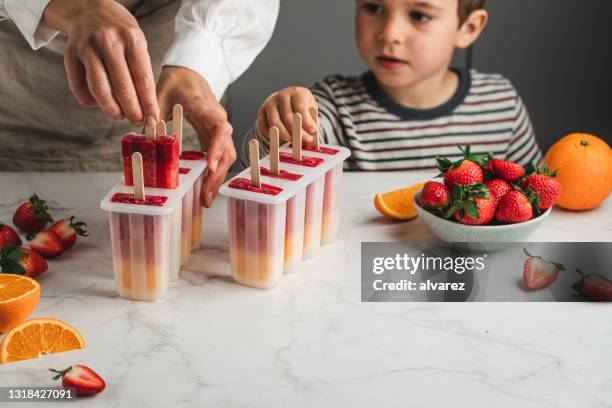 mujer e hijo haciendo paletas de hielo de naranja y fresa - préparation dessert fotografías e imágenes de stock