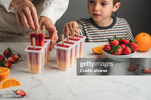 Donna e figlio che fanno scoppia il ghiaccio arancione e fragola Donna e figlio che fanno scoppia il ghiaccio arancione e fragola