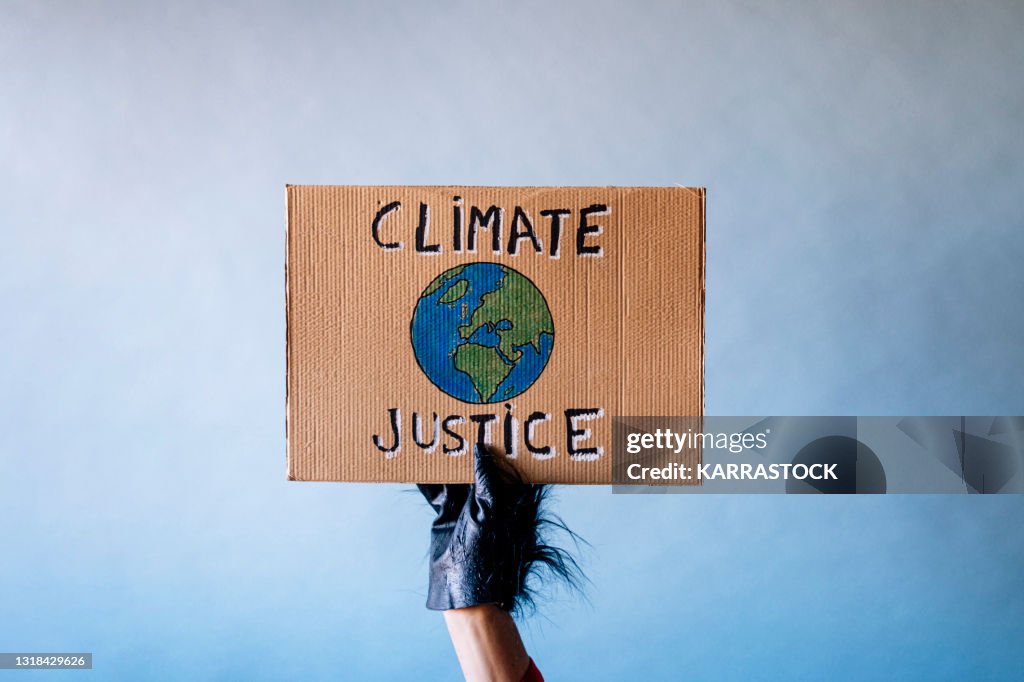 Man's hand dressed as a gorilla holding a cardboard sign that says CLIMATE JUSTICE