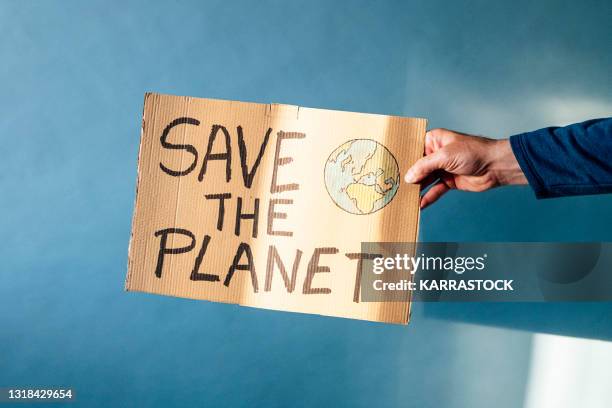 man's hand holding a cardboard sign that says save the planet - laboratory for the symptoms of global warming stockfoto's en -beelden
