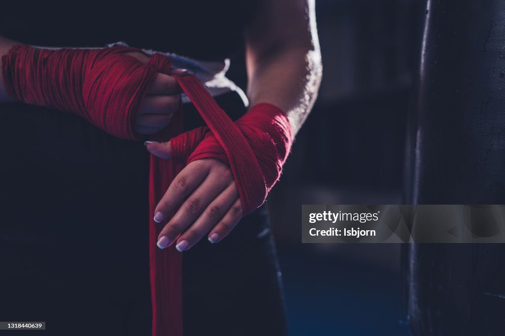 Unrecognizable female boxer applying adhesive bandage on hand before boxing training