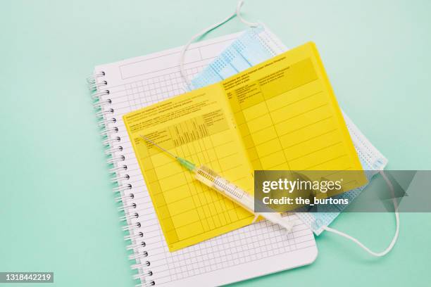 high angle view of a syringe, german vaccination certificate, surgical face mask and notepad on green background - yellow note pad stock pictures, royalty-free photos & images