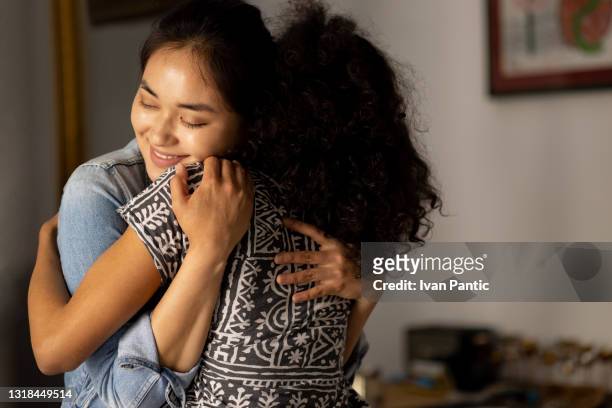 happy interracial couple of female friends hugging and smiling at home - repentant stock pictures, royalty-free photos & images