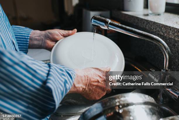 a man rinses a plate under a tap - kitchen sink stock pictures, royalty-free photos & images