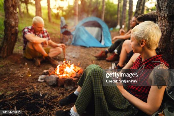 happy friends sitting next to the bonfire and telling stories - campfire storytelling stock pictures, royalty-free photos & images