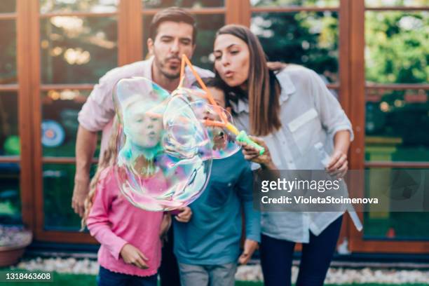 famiglia che si diverte nel cortile con bolle di sapone. - blowing bubbles foto e immagini stock