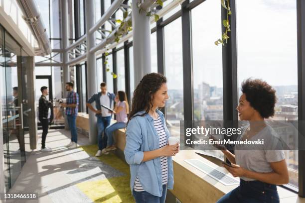 two female programmers using a digital tablet together in an office hallway - incidental people stock pictures, royalty-free photos & images