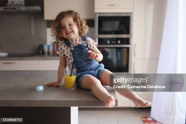 a 2 year old girl drinking a glass of orange juice in the kitchen - cute girl toddler imagens e fotografias de stock