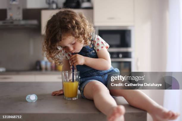 a 2 year old girl drinking a glass of orange juice in the kitchen - fruchtsaft stock-fotos und bilder