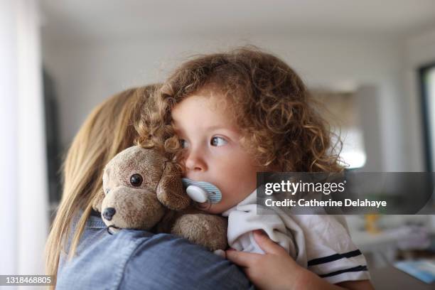 a 2 year old girl hugging her mum, with her pacifier and her teddy - 2 year old child fotografías e imágenes de stock