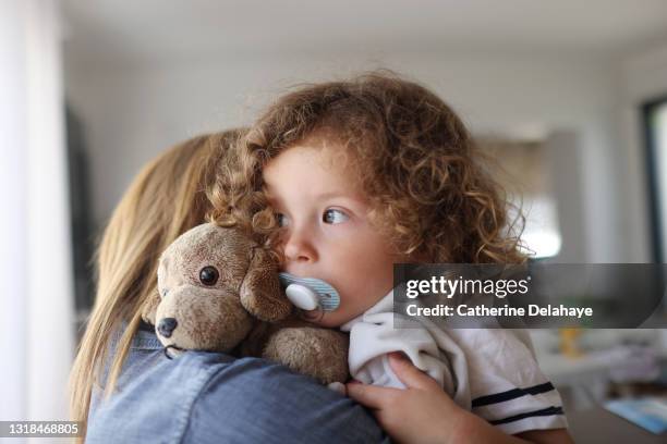 a 2 year old girl hugging her mum, with her pacifier and her teddy - babys dummy stock pictures, royalty-free photos & images