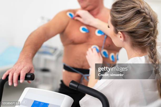 female doctor placing electrodes on the chest of a mature man - electrode stock pictures, royalty-free photos & images