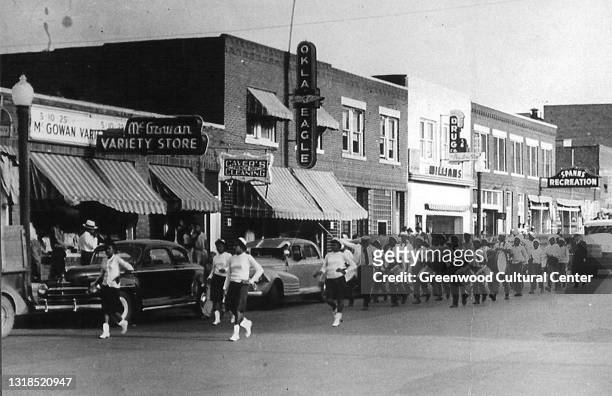 View of an unspecified parade on Greenwood Avenue, Tulsa, Oklahoma, 1930s or 1940s. Among the visible businesses are the offices of the Oklahoma...