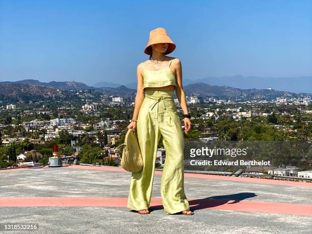 Julia Comil wears a lime sorbet cropped linen cami top by Bondi Born, lime sorbet high waisted linen pants by Bondi Born, an apricot Linen bucket hat...