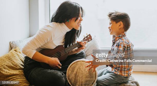 a young boy hits a drum as a woman holding a ukelele encourages him - songwriter stock pictures, royalty-free photos & images