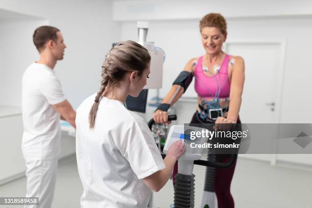 doctors overseeing the cardiopulmonary stress test taken by a woman on the bicycle - cardiopulmonary system stock pictures, royalty-free photos & images