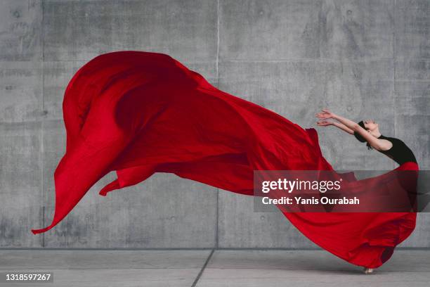 female ballet dancer on pointes dancing with a red veil in front of a grey concrete wall - rood stof stockfoto's en -beelden