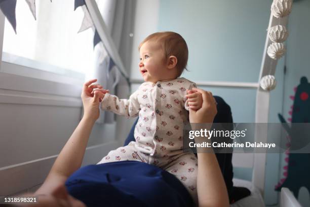 a 1 year old baby girl having fun in the arms of her mum at home - 30 year old portrait in house stock-fotos und bilder