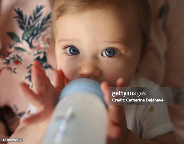 a 1 year old baby girl drinking her baby bottle of milk in the arms of her mum - milchflasche stock-fotos und bilder