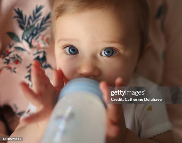 a 1 year old baby girl drinking her baby bottle of milk in the arms of her mum - drink bottle stock pictures, royalty-free photos & images