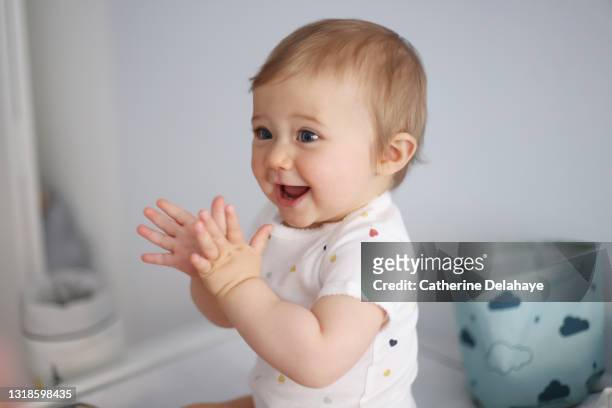 a 1 year old baby girl clapping her hands on her baby-changing table - bebé foto e immagini stock