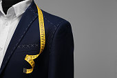 Semi-ready jacket with tailor's measuring tape on mannequin against grey background, closeup. Space for text