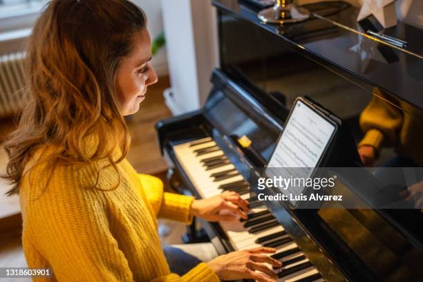 beautiful woman playing piano at home using digital tablet - piano stock pictures, royalty-free photos & images