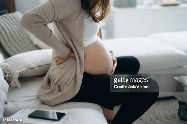 foto recortada de una mujer embarazada asiática tocándose el vientre y la espalda baja, sufriendo de dolor de espalda. salud del embarazo, concepto de bienestar - mujer embarazada fotografías e imágenes de stock