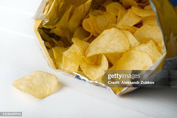 crispy fried greasy potato chips fall out or are spilled out of the package, on a white background or table. the concept of unhealthy diet and lifestyle, accumulation of excess weight. - chip stock-fotos und bilder